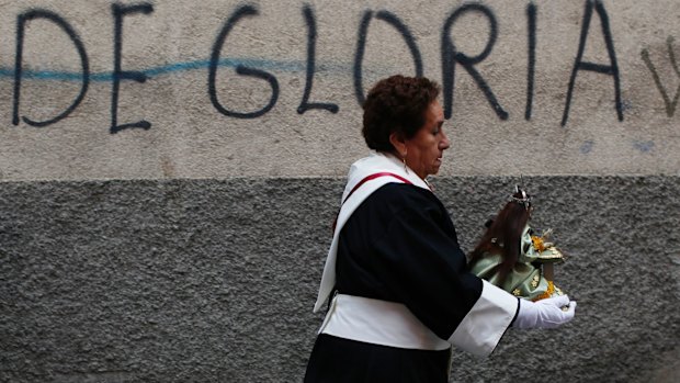 A woman in a penitent costume carries a small statue of Jesus to a Good Friday procession during Holy Week in La Paz, Bolivia.