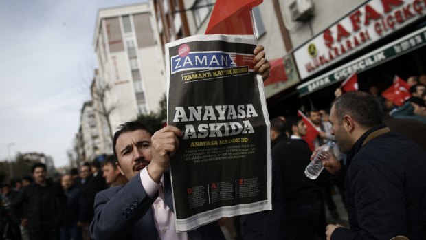 A man holds Saturday's copy of the newspaper which reads "the constitution suspended" as people gathered in support outside the headquarters of Zaman newspaper in Istanbul, on Sunday. 