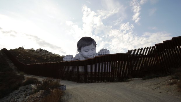 French artist JR, aiming to prompt discussions about immigration, erected a giant cut-out photo of a Mexican boy peering over a wall into the US from Tecate, California.