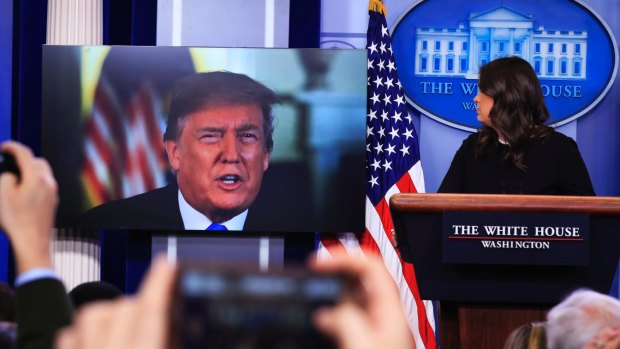 Donald Trump speaks via a video to journalists at a press briefing at the White House with press secretary Sarah Sanders at the lectern.  