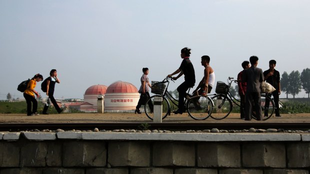People walk and cycle past a factory dome with writing which reads "First priority: self-development" in Hamhung, North Korea, on Thursday.