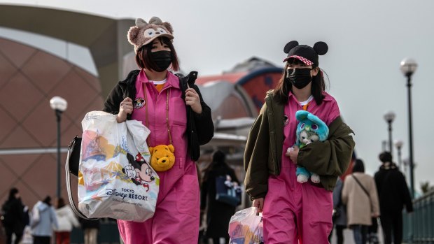 Women wearing face masks and novelty hats leave Tokyo Disneyland.