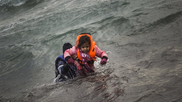 A man and his child - both wearing real life vests - struggle to shore after arriving at the Greek island of Lesbos. Two boats have capsized killing at least 43 refugees, including 17 children.