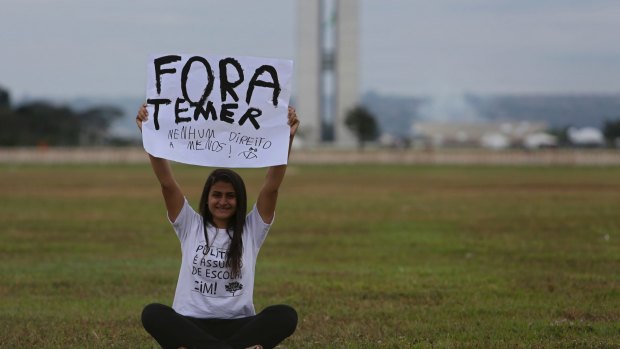 A woman holds up a poster with a message that reads in Portuguese; "Get out Temer, do not take any more of our rights" during an isolated protest in the center of Brasilia on Friday.
