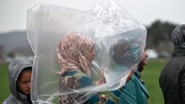 A migrant girl shields herself from the rain while waiting in a line for food rations at the northern Greek border station of Idomeni on Monday. 