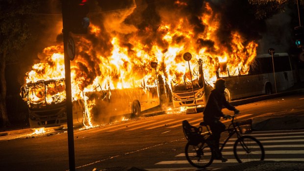 A man rides a bicycle past buses set on fire during a trade union general strike in Rio on Friday.