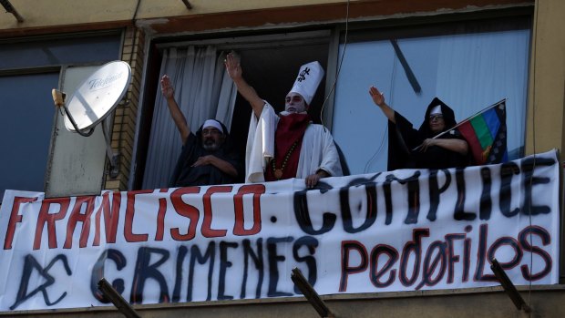 From a balcony in Santiago, protesters gesture and display a banner saying: "Francis, accomplice of paedophile crimes".