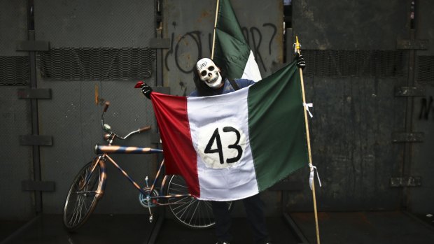A protester wearing a skull mask and holding a Mexican flag with its emblem covered with the number 43 stands in front of a police barrier during a march marking the one year anniversary of the disappearance of 43 rural college students in Mexico City on Saturday.