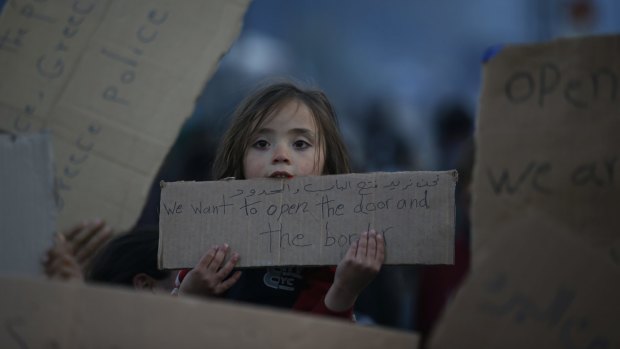 A migrant girl holds a sign pleading for open borders in Idomeni, Greece, on Saturday.