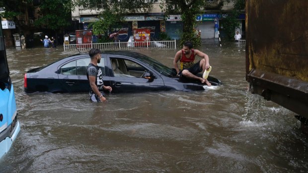 A man sits on a car that got stuck in a waterlogged street following heavy rains in Mumbai.