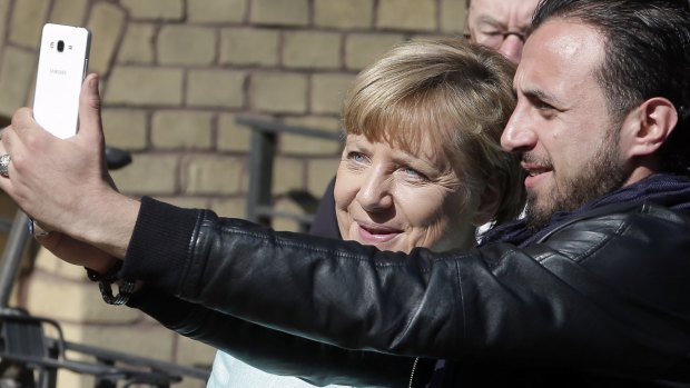 An unidentified man takes a picture of himself and German Chancellor Angela Merkel, left, during Merkel's visit to a registration centre for migrants and refugees in Berlin.