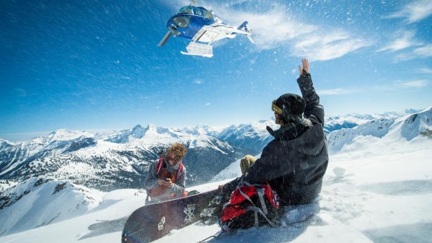 Snowboarders watch a helicopter take off after being
dropped on a remote peak in Revelstoke.