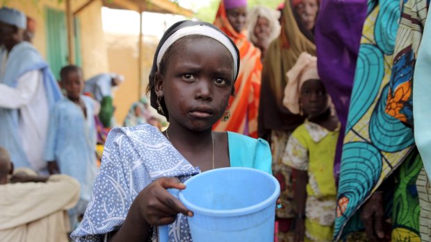 A girl drinks water as women queue for blankets and food from Nigerien soldiers in Damasak this week.