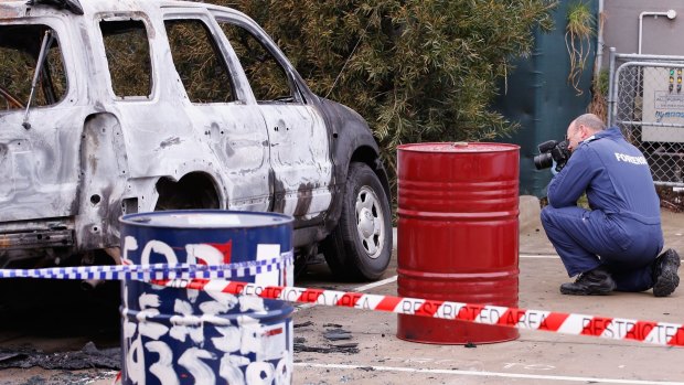 Forensic investigators photograph the burnt out car.