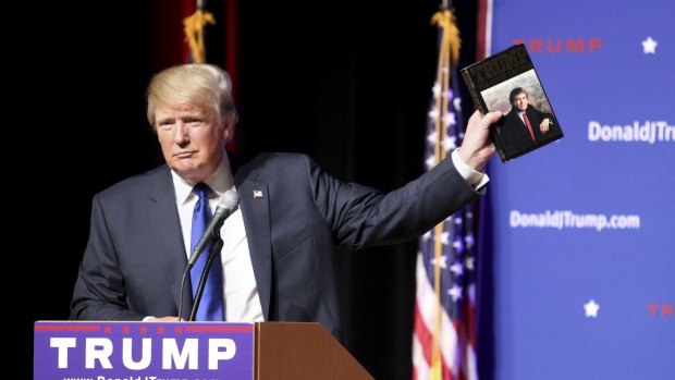 Donald Trump holds up a copy of his 1987 book, Trump: The Art of the Deal. 
