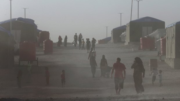 Displaced people who fled the battle between US-backed Syrian Democratic Forces and IS in Raqqa, walk in the dust at a refugee camp.