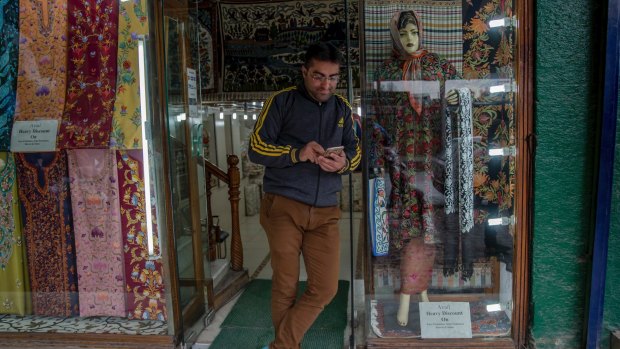 A Kashmiri shopkeeper browses the internet on his mobile phone he waits for customers outside his shop in Srinagar.