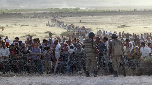 Turkish soldiers stand guard as Syrians wait behind the border fences near the southeastern town of Suruc in Sanliurfa province, on Thursday.