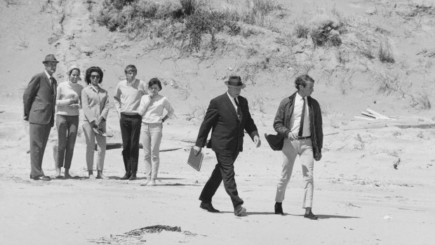Alan Stewart, who was with Harold Holt on the day he went missing, walks along Cheviot Beach with Commonwealth policeman A Jackman.