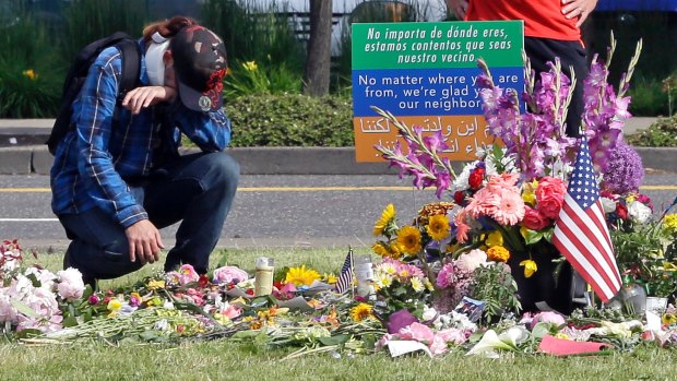 A mourner kneels in Portland at a memorial for the two men fatally stabbed last week next to a welcome message in English, Arabic and Spanish. 