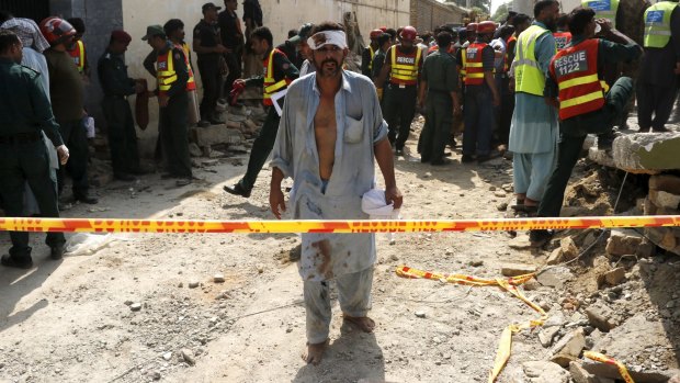 An injured man walks away as rescue workers search for survivors after a blast that killed provincial minister Shuja Khanzada in Attock on Sunday.
