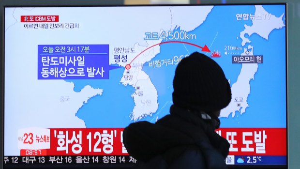 A man walks past a local news program in South Korea reporting on where the missile launch landed. 