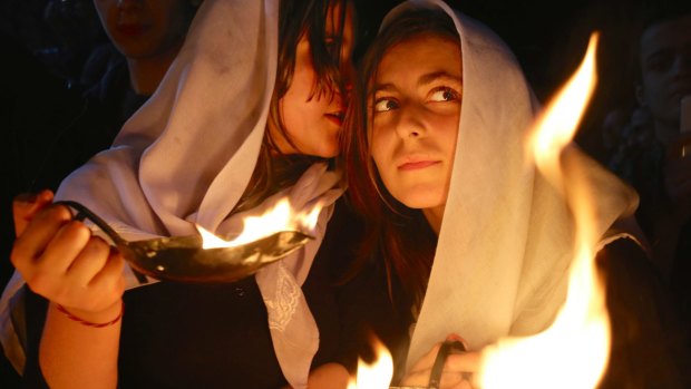 A Yazidi woman whispers into the ear of her friend as both hold small fires to make a wish for the Yazidi new year, at the holy shrine of Lalish, north of militant-held Mosul, Iraq.