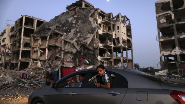 A Palestinian boy in a car drives past destroyed buildings in Beit Lahiya, northern Gaza Strip, in August 2014.