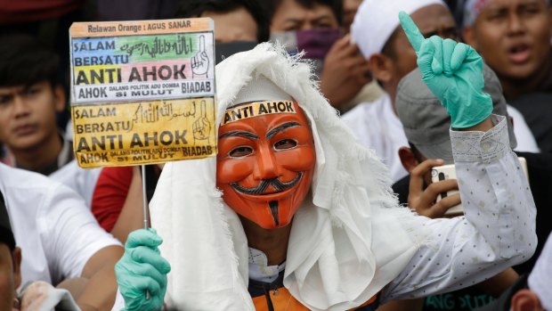 A masked man holds an anti-Ahok sign during a protest against governor Basuki "Ahok" Tjahaja Purnama at the main business district in Jakarta, Indonesia.
