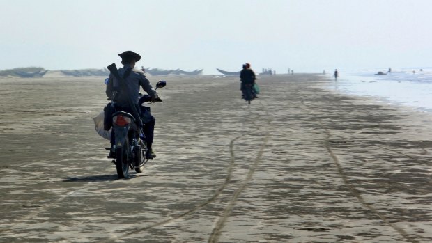 A police officer rides away with a bag of fish from Rohingya fishermen in Maungdaw.