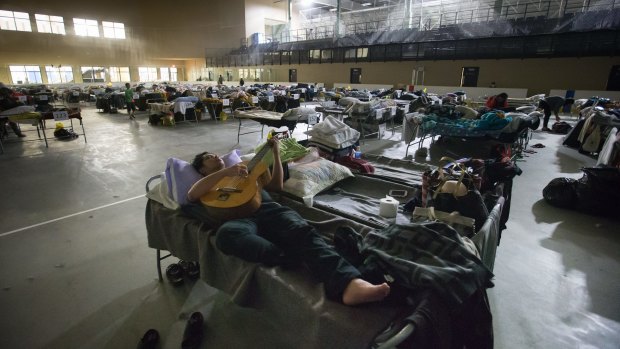 A Fort McMurray evacuee plays guitar while lying on a cot at a hockey rink in Lac La Biche, Alberta.