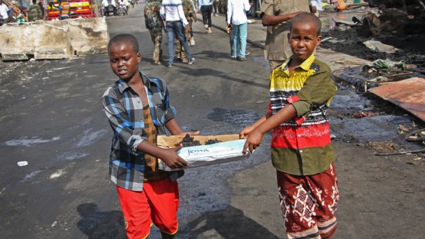 Somali children assist the effort to clear the bomb scene in Mogadishu by carrying away unidentified charred human remains in a cardboard box.