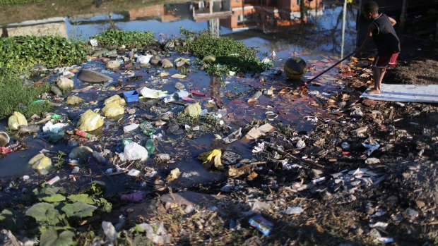 A boy reaches for a ball along a polluted canal in the Mare favela.