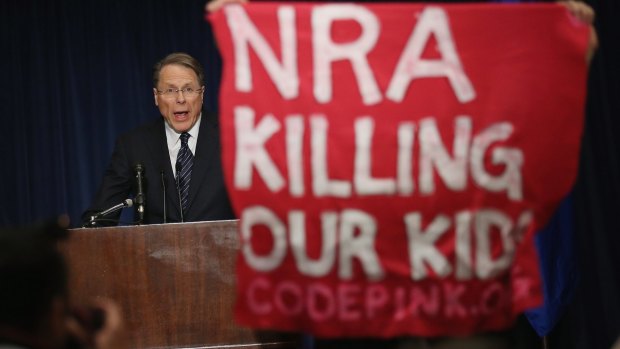 A demonstrator from an anti-gun lobby holds up a banner as NRA executive vice-president Wayne LaPierre speaks at a  news conference after the massacre at Sandy Hook Elementary School in Connecticut.