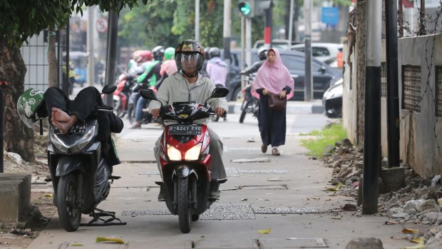 A motorcyclist rests on his bike as another passes him on a footpath in Jakarta on Tuesday. 