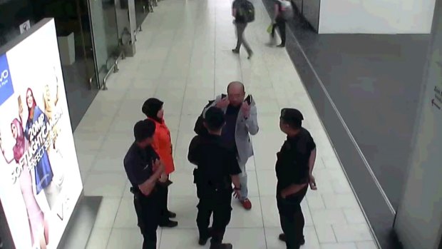 In this image from security camera footage, Kim Jong-nam, in grey, gestures towards his face while talking to airport security at Kuala Lumpur International Airport, shortly before his death.