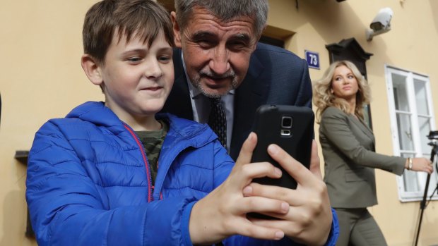 Czech billionaire Andrej Babis, takes a photo with a child as his wife Monika, right, leaves a polling station after casting his vote.