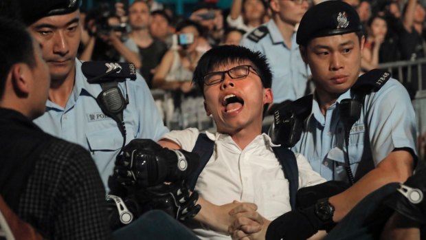 Pro-democracy activist Joshua Wong is detained by police officers after climbing the Golden Bauhinia on Wednesday.