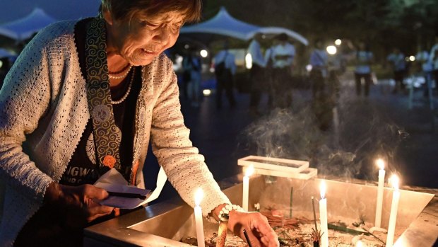 A woman lights a candle as she prays for the atomic bomb victims in front of the cenotaph at the Hiroshima Peace Memorial Park.