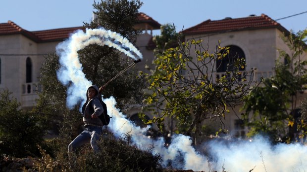 Return to sender: A Palestinian hurls a smoke grenade back at Israeli soldiers during clashes in the West Bank.