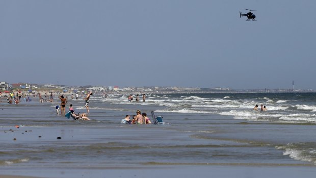 A helicopter flies close to the water as vacationers relax on the beach in Oak Island, a day after two teenagers were attacked by a shark. 