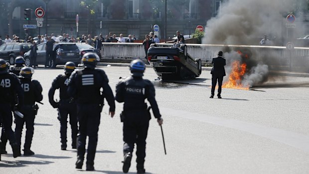 French riot police stand next to an overturned car in Paris.