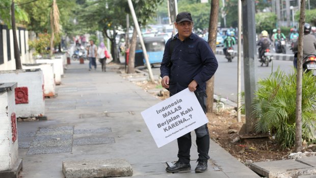 Alfred Sitorus from the Coalition of Pedestrians in Jakarta holding a placard that says: "Indonesians are lazy walking because ....?".