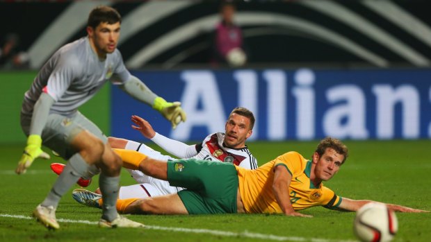 Socceroos Mat Ryan and Luke DeVere watch a cross go past as Germany's Lukas Podolski slides in the background.