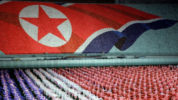 North Koreans perform with scarves below the North Korean flag.