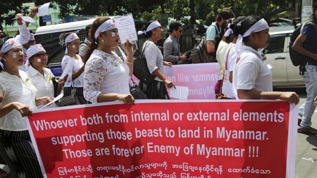 Protesters in Myanmar hold a placard describing migrants in the Bay of Bengal as beasts.