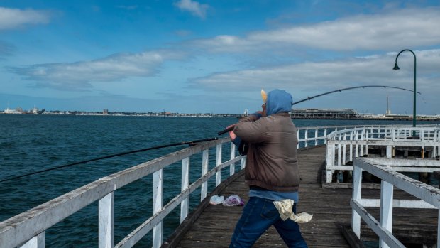 A lone fisherman braves the unseasonably cool summer weather at Port Melbourne.