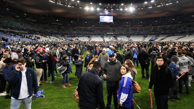 Terrified: Spectators gather on the pitch at Stade de France after news of the bombing and terrorist attacks reached the fans.