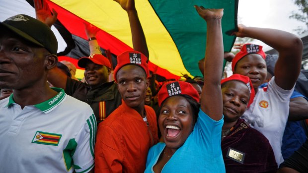 Protesters raise their fists under a large national flag, at a demonstration of tens of thousands at Zimbabwe Grounds in Harare.