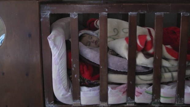 Make-do: Six-month-old Kareema sleeps in a borrowed cot, blankets piled high in an attempt to keep out the cold.
